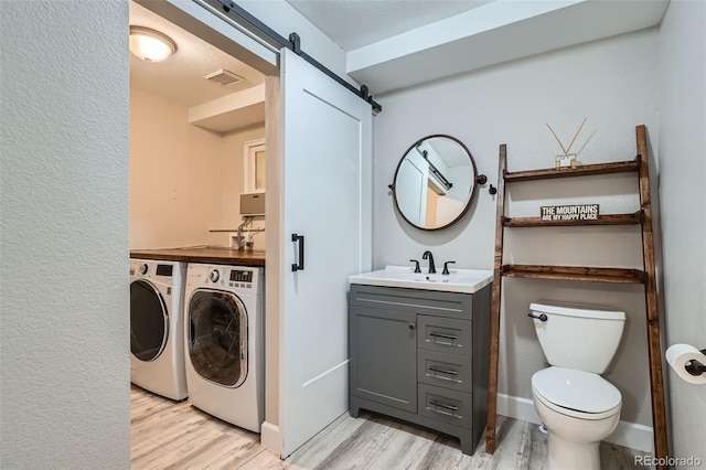 washroom featuring a barn door, sink, washer and clothes dryer, and light wood-type flooring