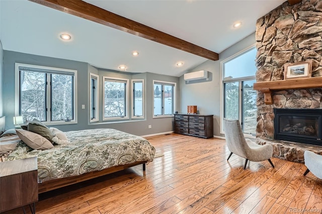 bedroom featuring a wall mounted AC, a fireplace, light hardwood / wood-style flooring, multiple windows, and vaulted ceiling with beams