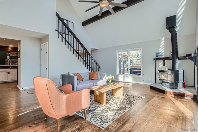 living room with sink, a wood stove, dark hardwood / wood-style flooring, ceiling fan, and high vaulted ceiling