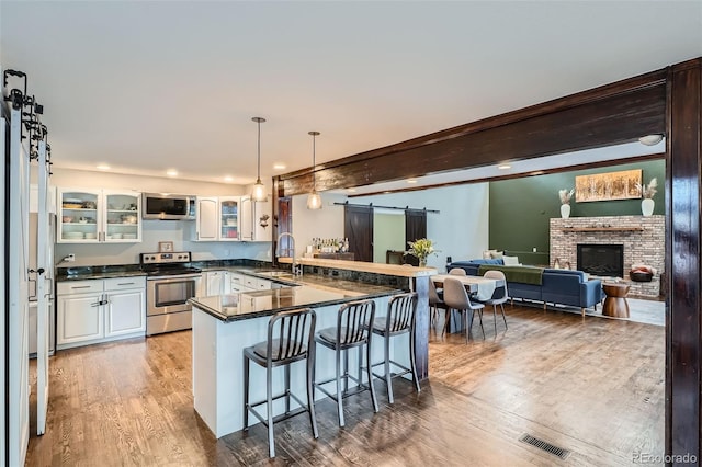 kitchen with appliances with stainless steel finishes, a kitchen breakfast bar, a barn door, kitchen peninsula, and white cabinets