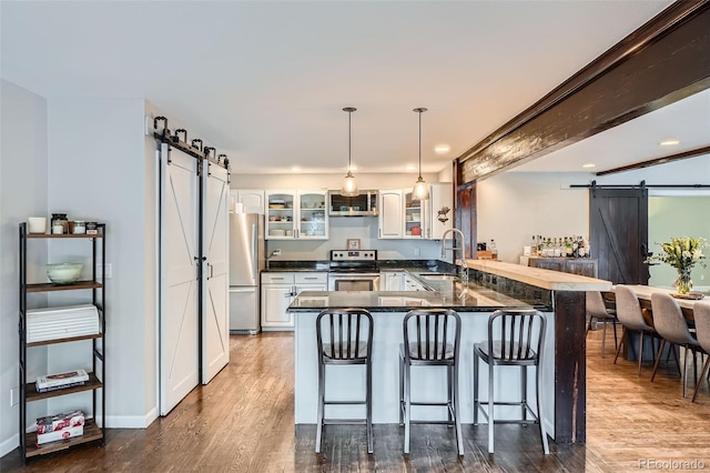 kitchen with white cabinets, appliances with stainless steel finishes, a barn door, and kitchen peninsula