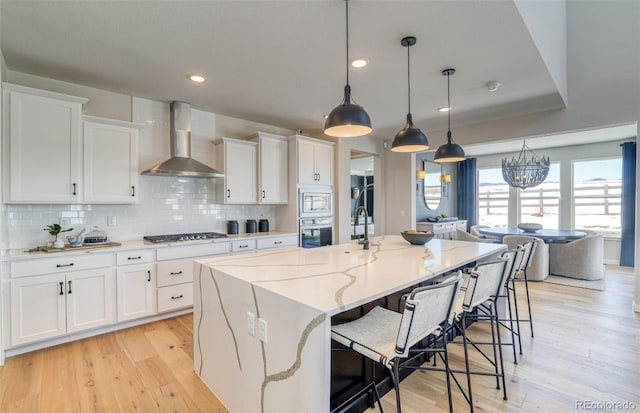 8576 Hotchkiss St, Littleton, CO 80125 - kitchen featuring light wood finished floors, decorative backsplash, appliances with stainless steel finishes, white cabinets, and wall chimney exhaust hood