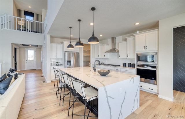 8576 Hotchkiss St, Littleton, CO 80125 - kitchen with a breakfast bar area, stainless steel appliances, white cabinetry, light wood-style floors, and wall chimney range hood