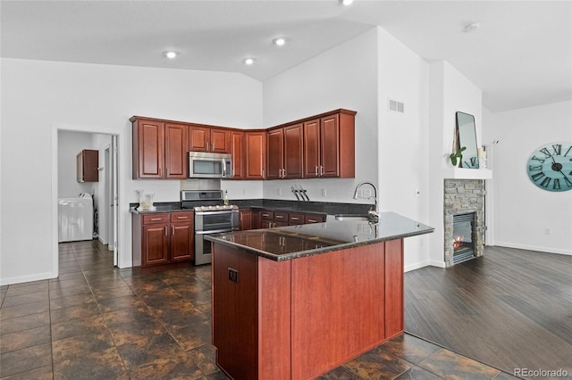 kitchen with a stone fireplace, sink, high vaulted ceiling, appliances with stainless steel finishes, and kitchen peninsula