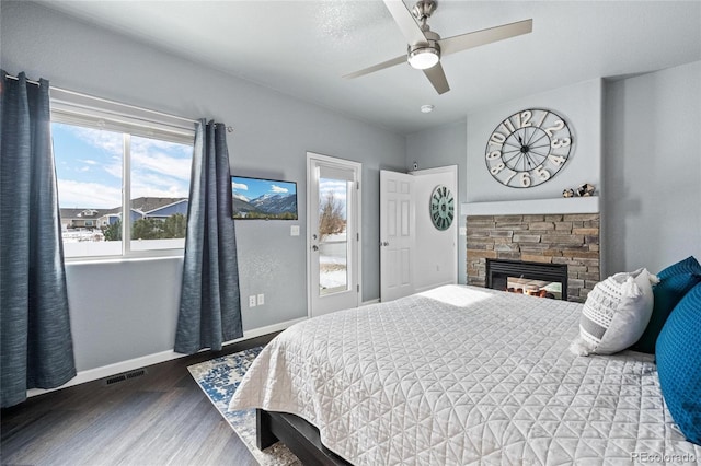 bedroom featuring a stone fireplace, wood finished floors, a ceiling fan, visible vents, and baseboards