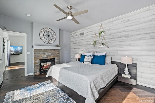 bedroom with visible vents, baseboards, ceiling fan, wood finished floors, and a stone fireplace