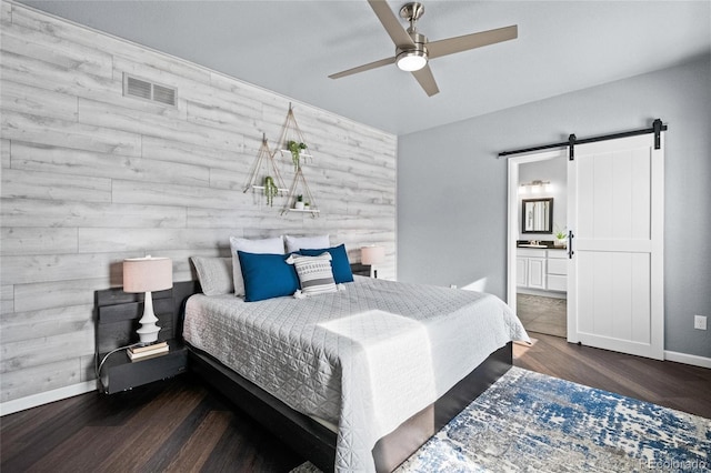 bedroom featuring ceiling fan, a barn door, connected bathroom, and wooden walls