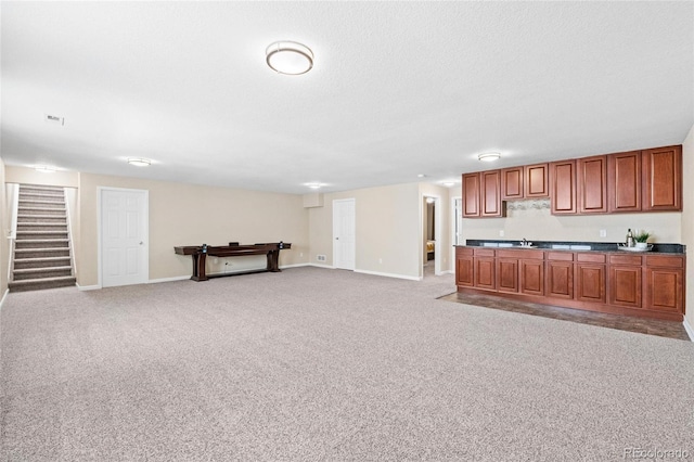 kitchen featuring light carpet, baseboards, brown cabinets, open floor plan, and a sink