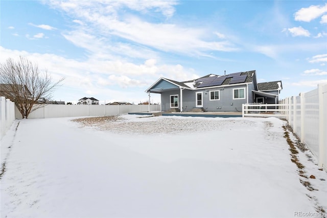 snow covered back of property with solar panels and a fenced backyard