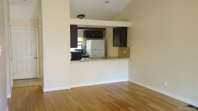 kitchen with white refrigerator, kitchen peninsula, light hardwood / wood-style floors, and vaulted ceiling