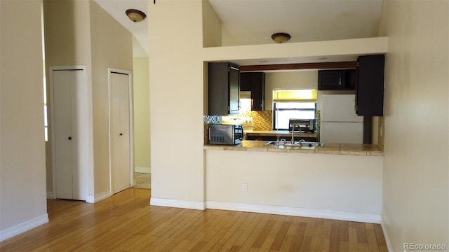 kitchen with sink, kitchen peninsula, wood-type flooring, backsplash, and white fridge