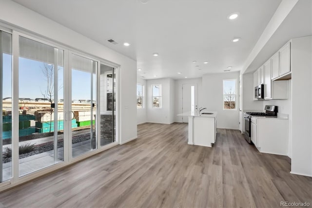 kitchen featuring an island with sink, white cabinetry, sink, stainless steel appliances, and light wood-type flooring