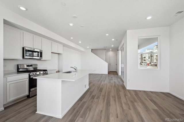 kitchen featuring sink, stainless steel appliances, white cabinets, a center island with sink, and light wood-type flooring