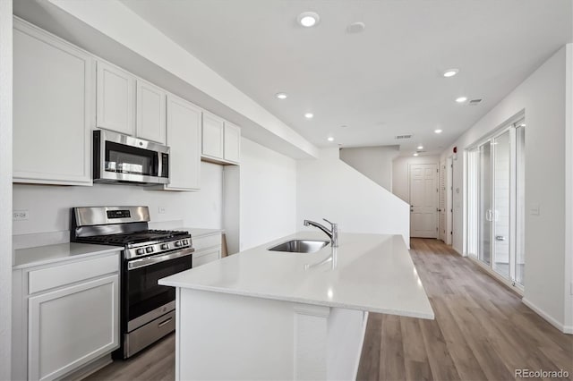 kitchen with white cabinetry, sink, stainless steel appliances, and an island with sink