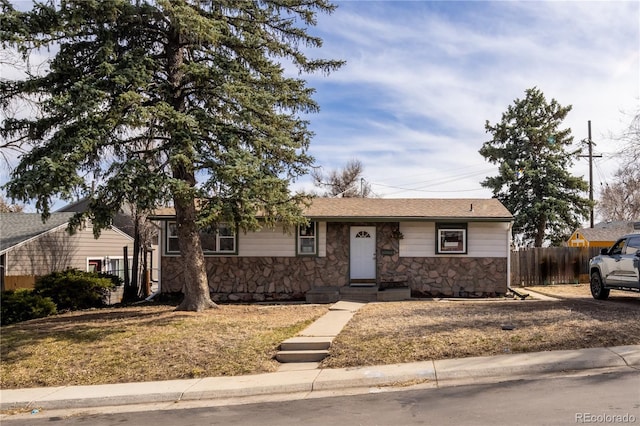 single story home featuring stone siding and fence