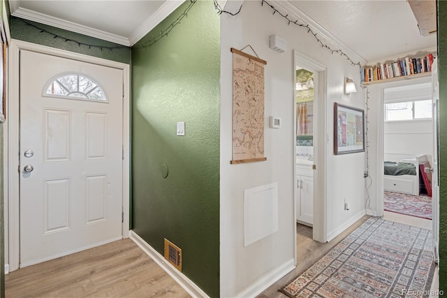 entrance foyer with light wood finished floors, visible vents, crown molding, and baseboards