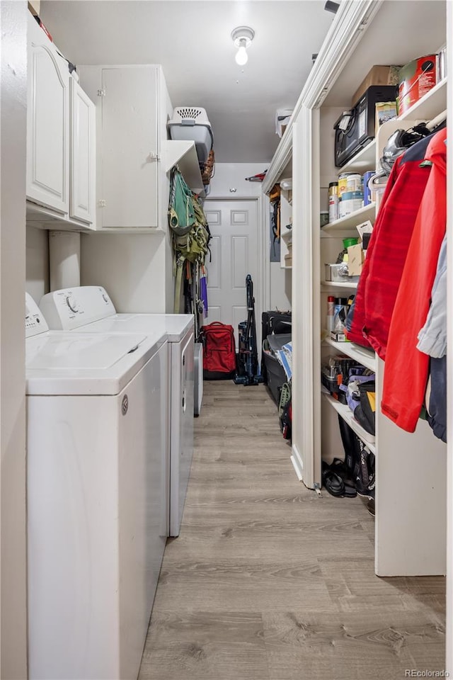 clothes washing area featuring washing machine and clothes dryer, cabinet space, and light wood-type flooring