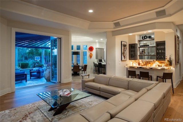 living room featuring light wood-type flooring, a tray ceiling, and bar