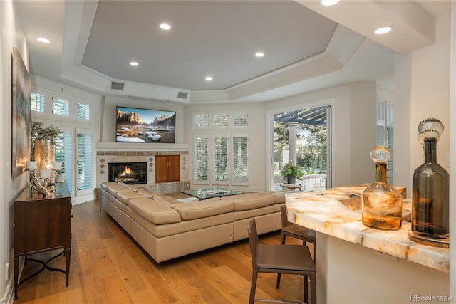 living room with a raised ceiling, a fireplace, and light hardwood / wood-style floors