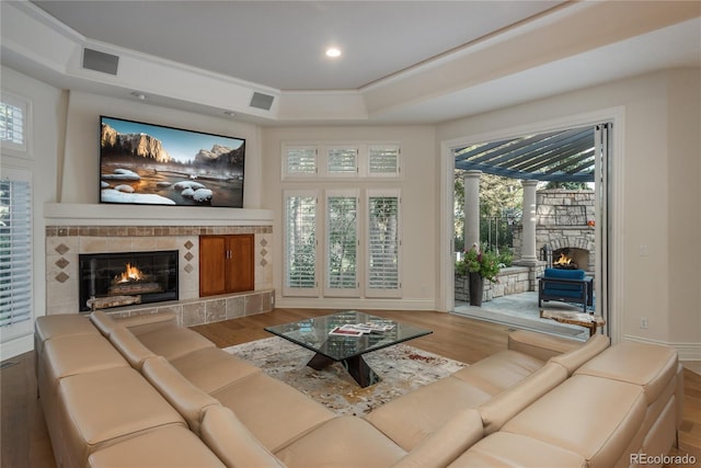 living room featuring a tile fireplace, light hardwood / wood-style flooring, and a raised ceiling