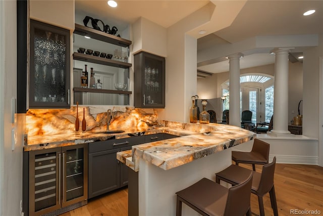 bar featuring beverage cooler, backsplash, light wood-type flooring, and sink