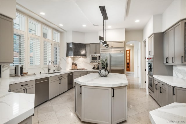 kitchen with gray cabinets, built in appliances, hanging light fixtures, and a kitchen island