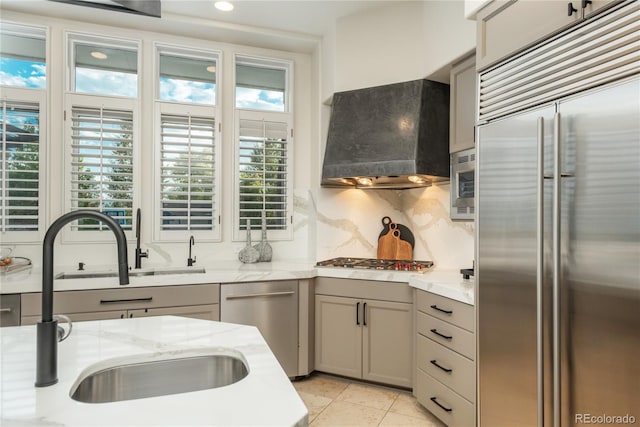 kitchen featuring built in appliances, wall chimney exhaust hood, sink, and a wealth of natural light