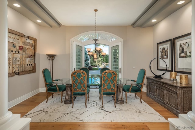 dining room with light wood-type flooring, decorative columns, and a notable chandelier