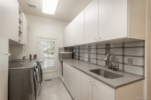 kitchen with washing machine and dryer, white cabinetry, sink, and light tile patterned floors