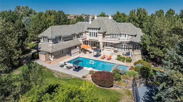 rear view of property featuring a yard, a balcony, a swimming pool with hot tub, and a patio area