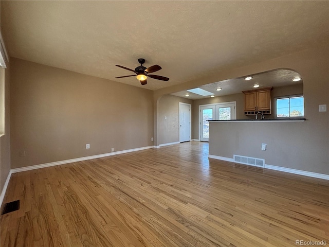 unfurnished living room featuring arched walkways, visible vents, light wood-style flooring, and baseboards