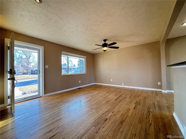 unfurnished living room with ceiling fan, a textured ceiling, wood-type flooring, and baseboards