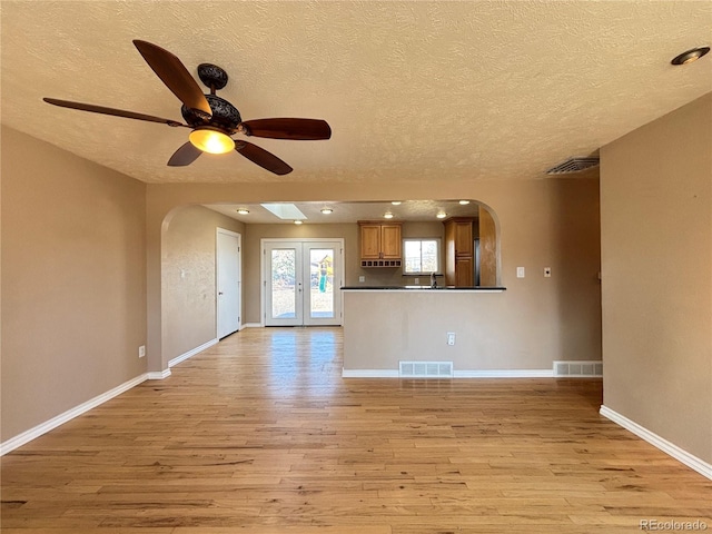 unfurnished living room featuring arched walkways, light wood-type flooring, and visible vents