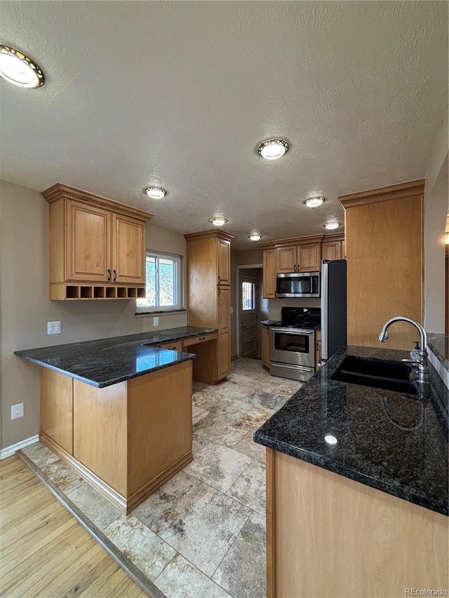 kitchen with a peninsula, a sink, baseboards, appliances with stainless steel finishes, and dark stone countertops