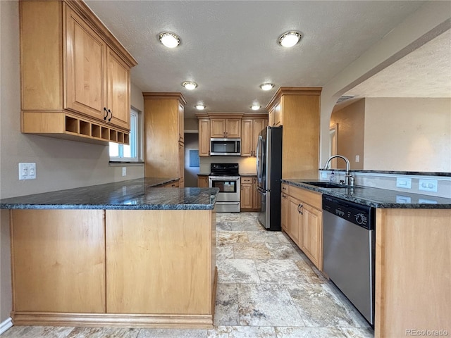 kitchen featuring arched walkways, stainless steel appliances, a peninsula, a sink, and dark stone countertops