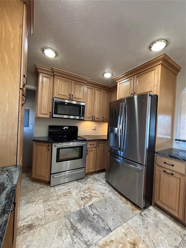 kitchen featuring dark stone counters, appliances with stainless steel finishes, a textured ceiling, and brown cabinets