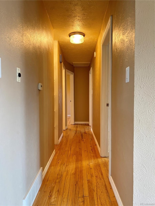 hall with light wood finished floors, baseboards, visible vents, and a textured ceiling