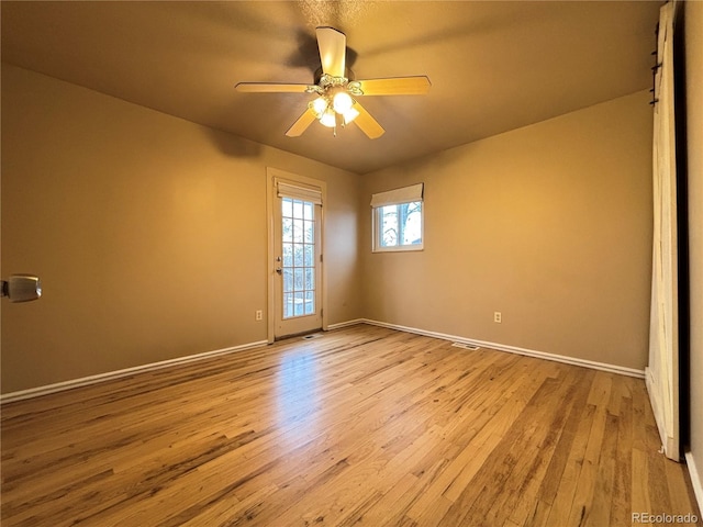 empty room with light wood finished floors, a ceiling fan, and baseboards