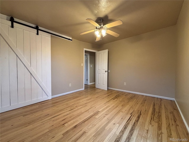 interior space featuring baseboards, ceiling fan, light wood finished floors, and a barn door