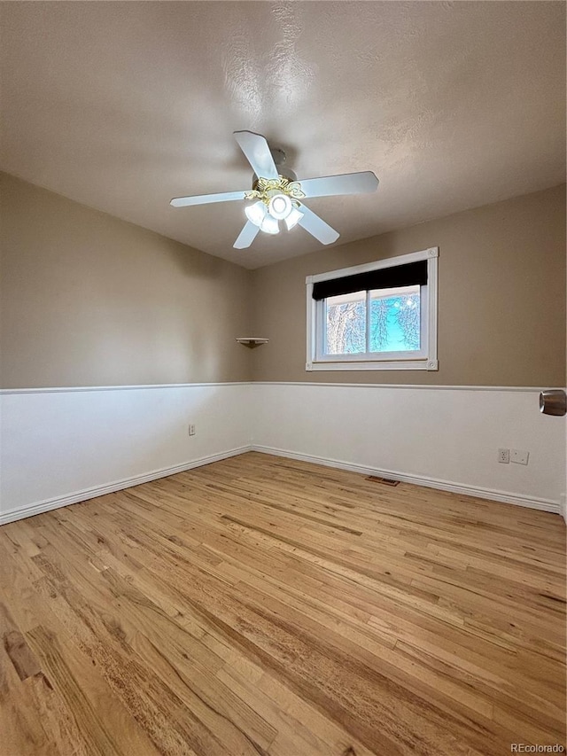 unfurnished room featuring visible vents, wood finished floors, a ceiling fan, and baseboards