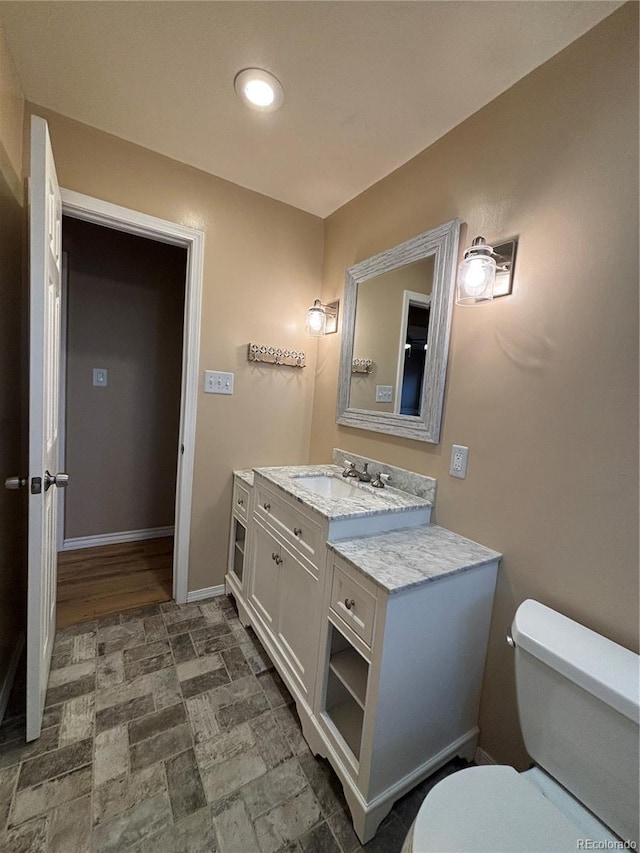 half bath featuring stone finish floor, baseboards, vanity, and toilet