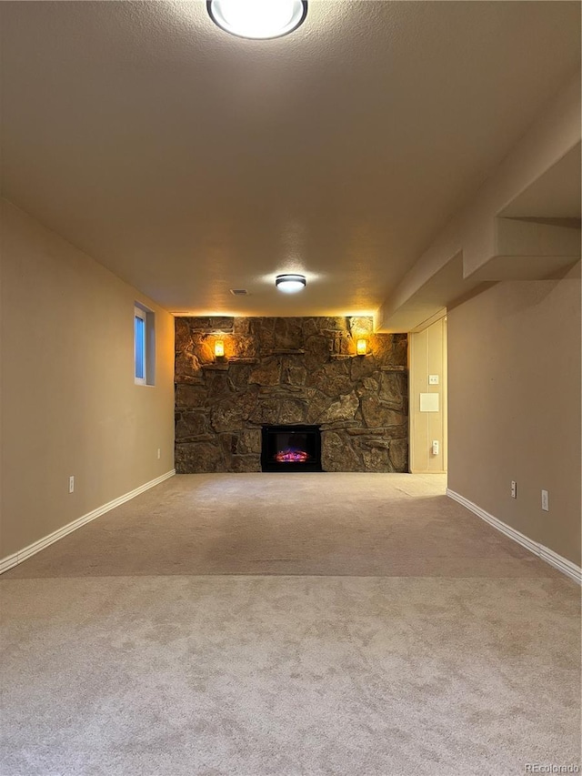 finished basement with carpet floors, a stone fireplace, baseboards, and a textured ceiling