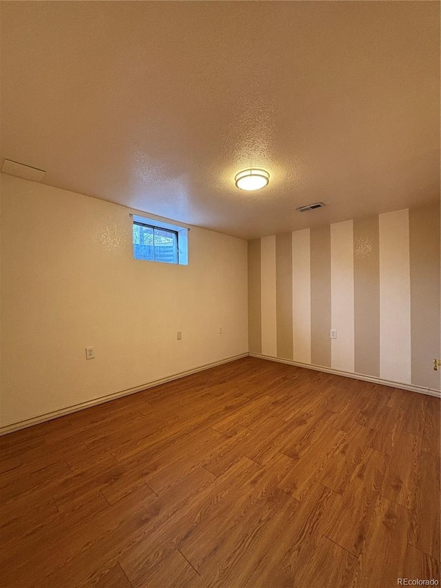 below grade area featuring visible vents, a textured ceiling, baseboards, and wood finished floors