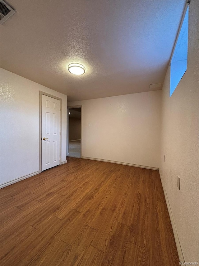 spare room featuring a textured ceiling, a textured wall, wood finished floors, visible vents, and baseboards