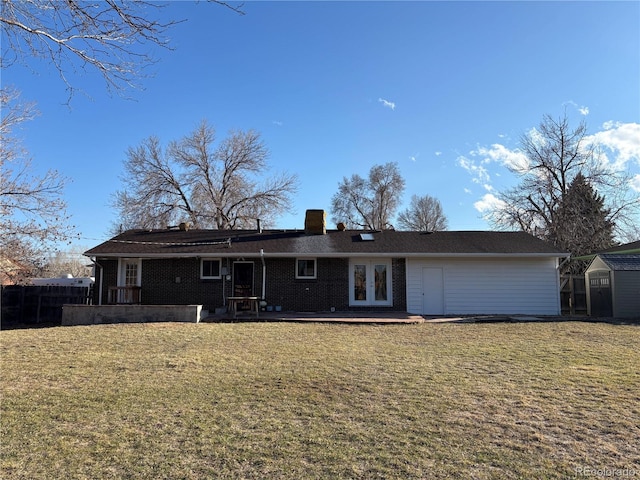 rear view of house with french doors, a chimney, a storage unit, a lawn, and an outdoor structure