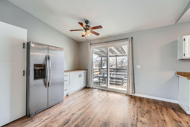 kitchen featuring light wood-type flooring, stainless steel fridge, vaulted ceiling, and white cabinets