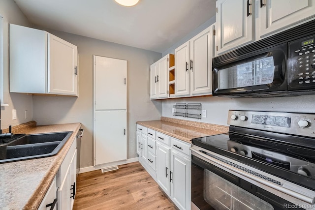 kitchen with black microwave, white cabinets, light countertops, light wood-type flooring, and stainless steel range with electric stovetop