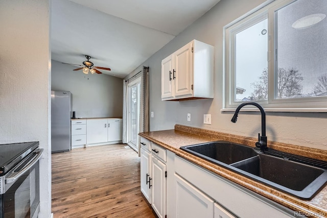 kitchen featuring ceiling fan, appliances with stainless steel finishes, light wood-style floors, white cabinetry, and a sink