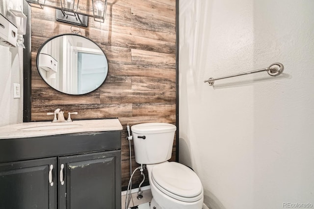 bathroom featuring toilet, wooden walls, and vanity