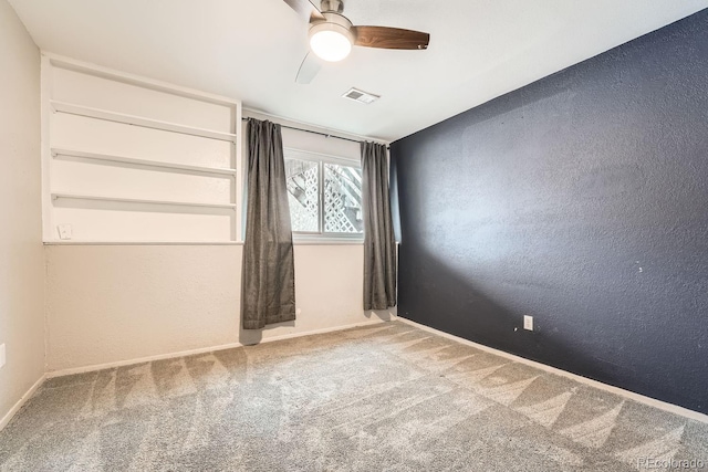 carpeted spare room with ceiling fan, a textured wall, visible vents, and baseboards